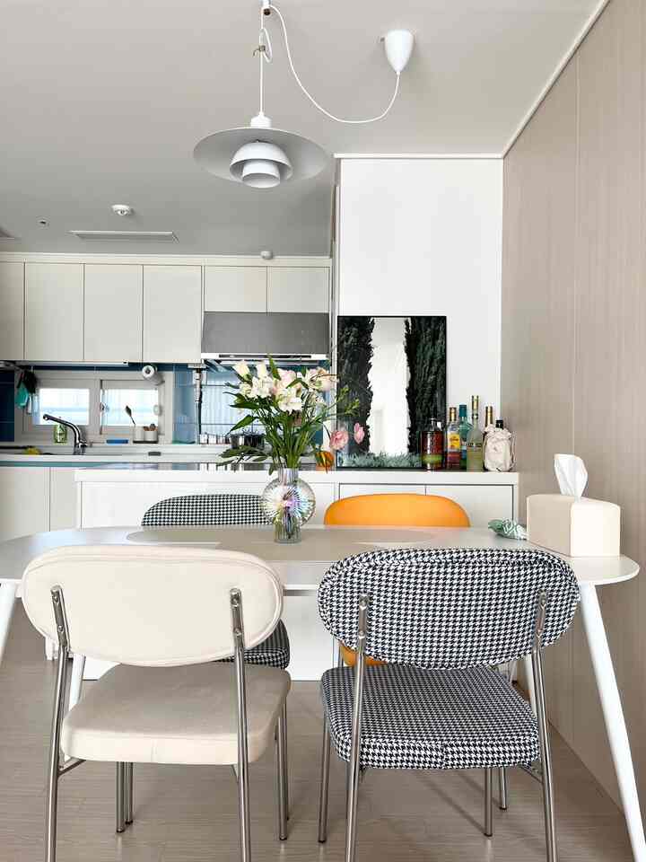 Modern dining room with white and black tones, featuring a white dining table and chairs, pendant light, and flower vase in a clean space