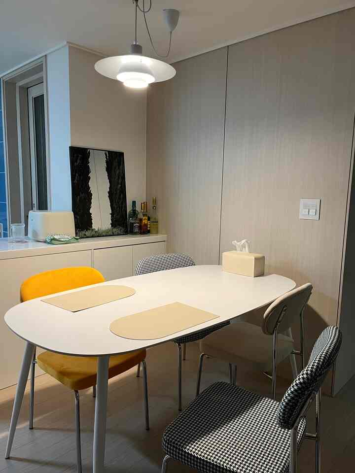 アイボリーとホワイトのトーンのダイニングルーム、カラフルな椅子とペンダントライトが配置されたモダンで居心地の良い空間