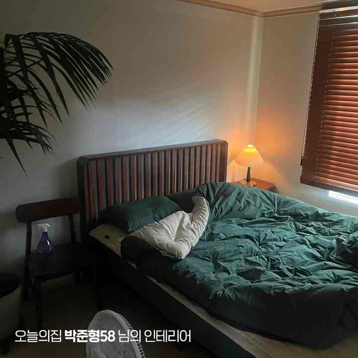 白い壁と茶色の木製ブラインド、ナチュラルな木のベッドフレームと緑の布団カバーが配置された雰囲気のある寝室インテリア