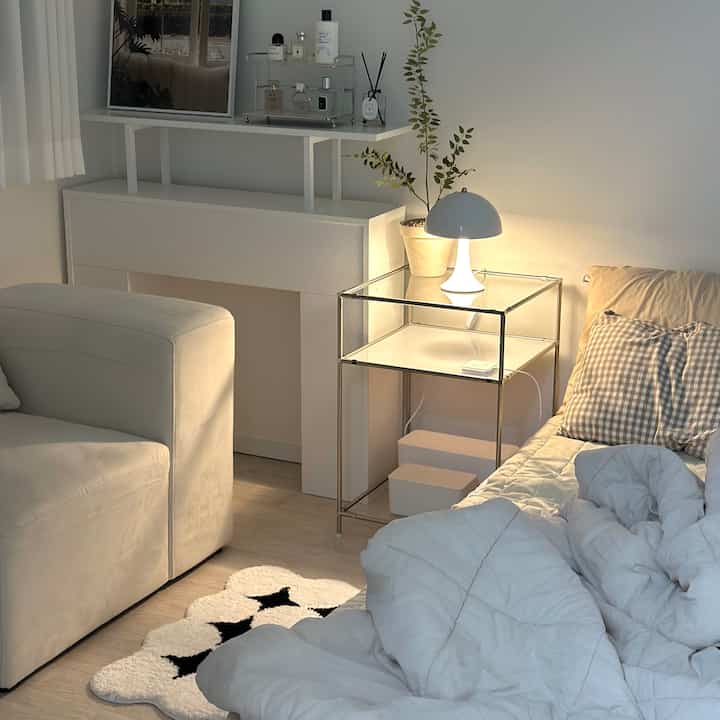 White and natural toned bedroom featuring transparent nightstand and table lamp creating a cozy atmosphere