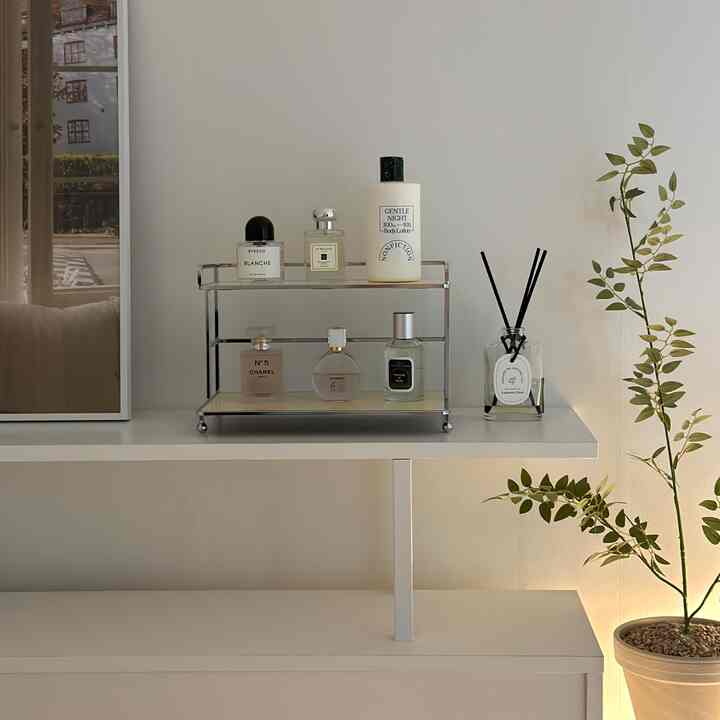 白色を基調とした寝室に、ミニ2段棚と香水、ディフューザー、観葉植物が配置されたシンプルで自然な雰囲気のインテリア
