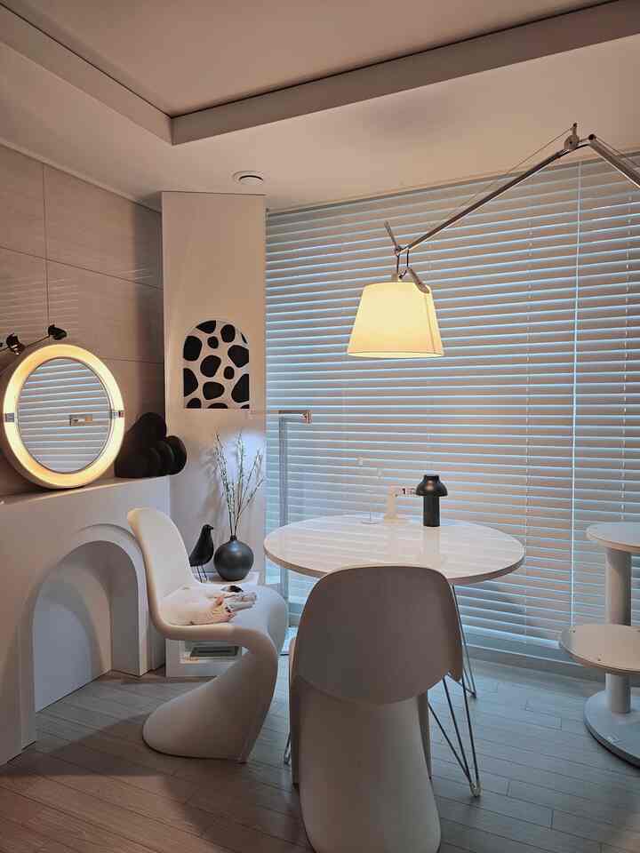 White-toned living room with round dining table and chairs, blinds covering window, showcasing modern and simple space with a cat napping on a chair