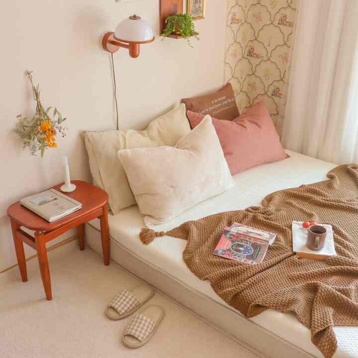 Beige and brown toned small bedroom featuring cozy bed, wall sconce, and decor items creating a comfortable atmosphere