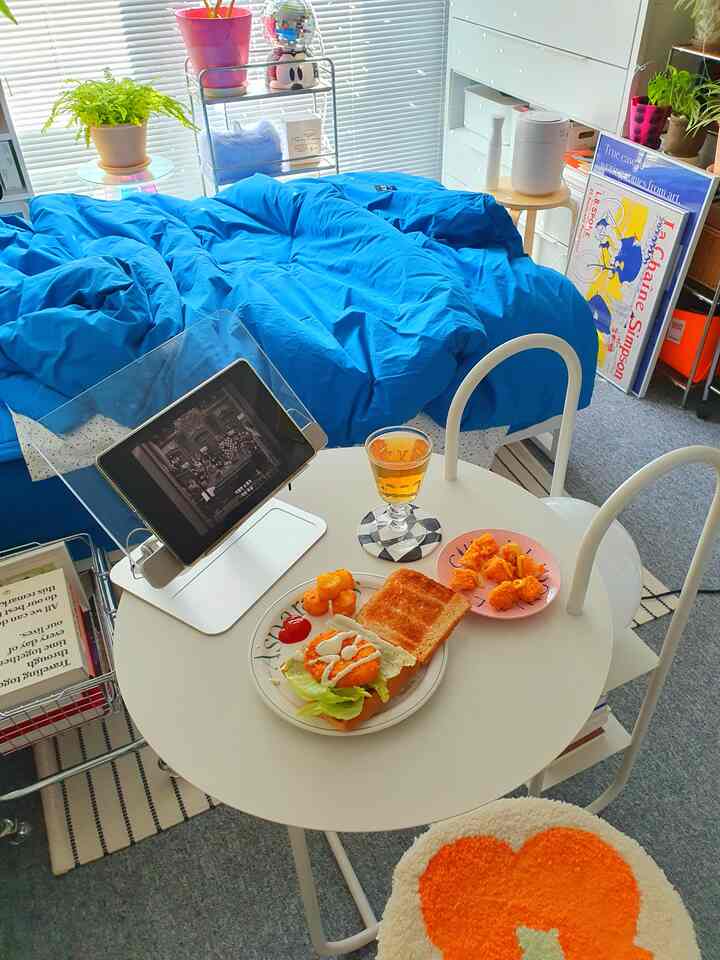 明るいホワイトとブルーの色調のコンパクトなワンルーム、中央にテーブルとベッドが配置された雰囲気のあるリラクゼーション空間