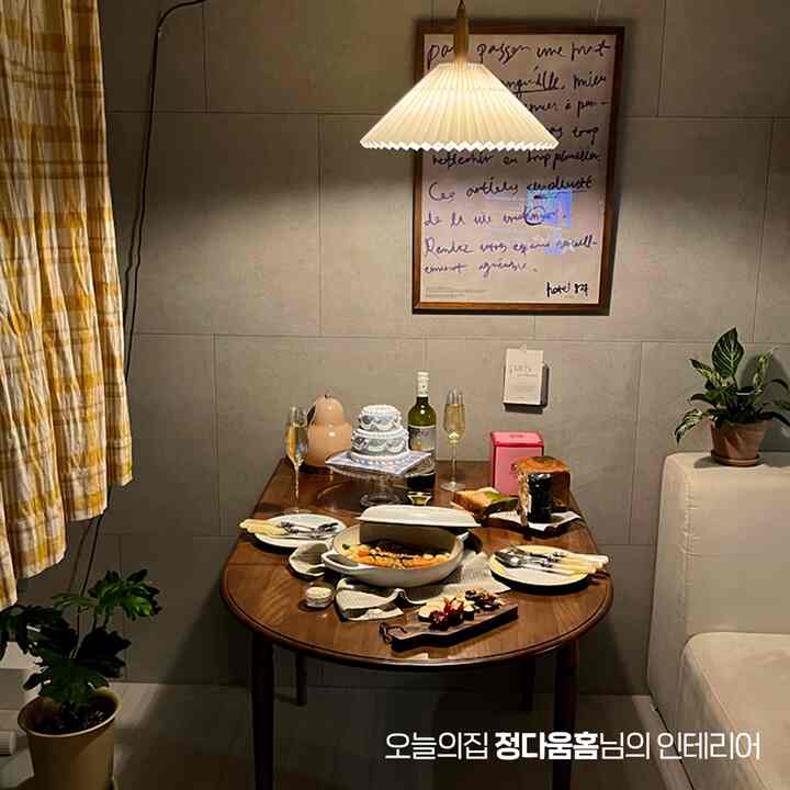 ホワイトとブラウンの色調のリビング兼ダイニング空間で、木製テーブル、ポスター、食器、植物が配置された雰囲気のあるインテリア