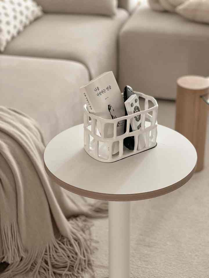 Ivory and beige toned living room featuring simple sofa and side table with a ceramic basket organizing remotes and a book