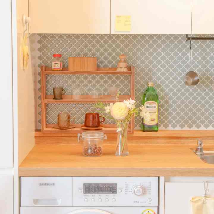 Natural wood-toned kitchen with gray tiled backsplash, featuring a vase with flowers and wooden storage shelf creating a clean atmosphere