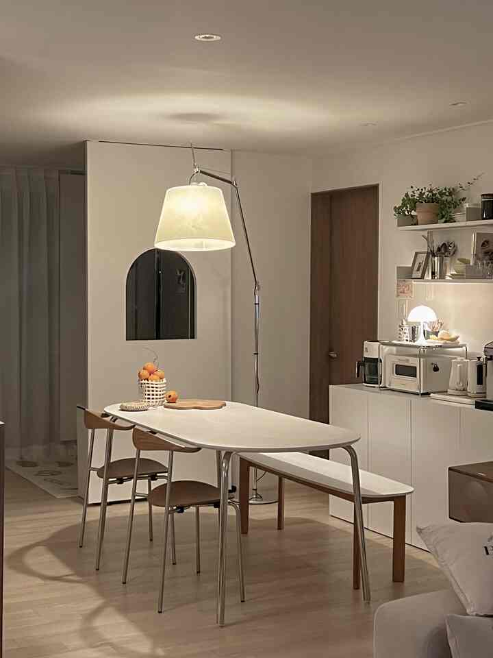 白と木目調の調和したモダンなキッチン空間、アーテミデ・トロメオ・メガのフロアランプがダイニングテーブル上に置かれ、温かみのある雰囲気を演出するインテリア