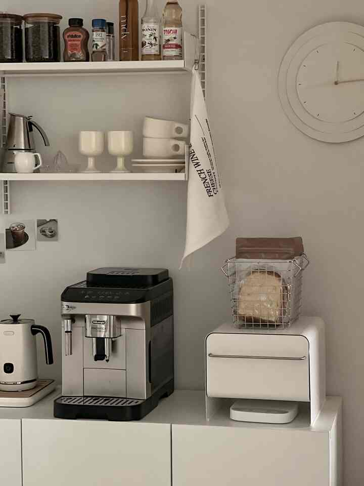 Bright white-toned kitchen space featuring a stainless coffee machine, white cabinets, and kitchen cloth, creating a cozy atmosphere