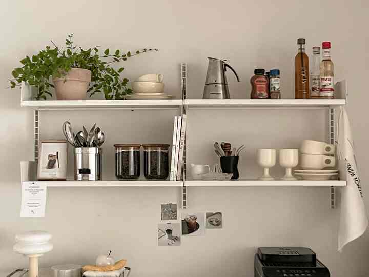 ナチュラルな色調のキッチン、白い棚にボウルやカトラリー、グラスが整然と配置された雰囲気のあるインテリア