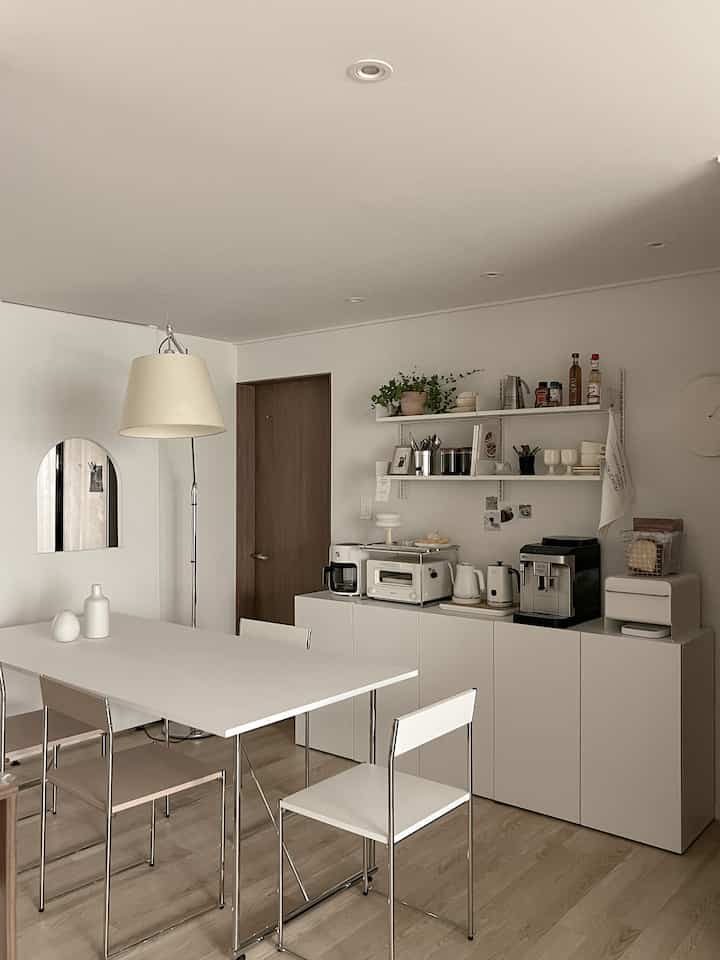 Natural modern kitchen space featuring white and wood tones, simple table and chairs, with coffee machine and toaster creating a cozy atmosphere