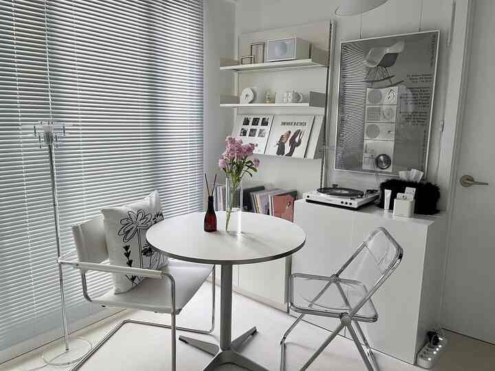 Softly lit white-tone dining room featuring a round table, transparent chairs, vinyl records, and audio equipment in a modern setting