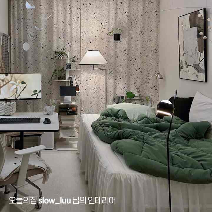 ベージュのカーテンと白い寝室、緑の寝具とコンピューターデスクが配置されたシンプルモダンな一人暮らしの空間