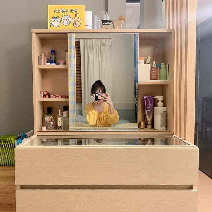 Beige and wood tone studio apartment vanity space featuring sliding storage mirror and island cabinet with tidy organization