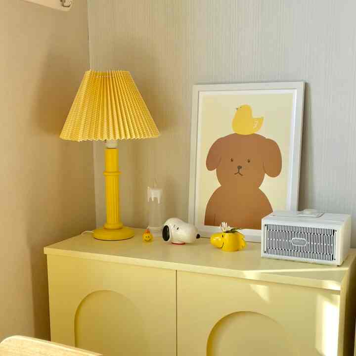 Warm yellow-toned studio space featuring a pleated yellow table lamp and a cute dog poster, creating a cozy baby room atmosphere