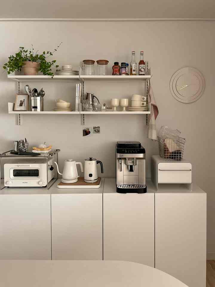 White-toned kitchen featuring neat white cabinets and shelves with coffee appliances in a simple setting
