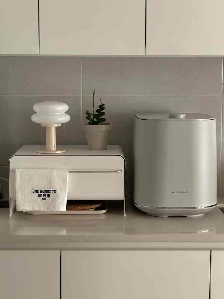 白とベージュのトーンのキッチン、収納ケースとテーブルランプが配置されたミニマルで落ち着いた雰囲気のインテリア