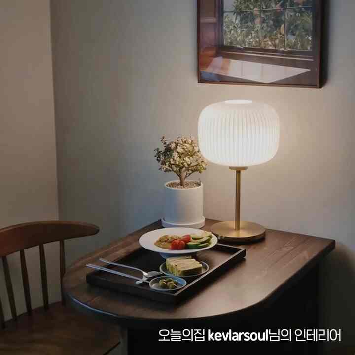 ナチュラルな色調のダイニング、木製のテーブルと椅子、白いテーブルランプと植物、簡単な朝食が置かれた雰囲気のあるインテリア