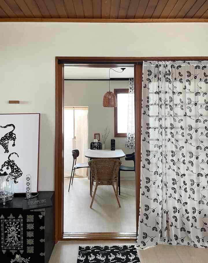 White and wood tone kitchen featuring a rattan chair, dining table, and sheer floral curtains with a natural atmosphere