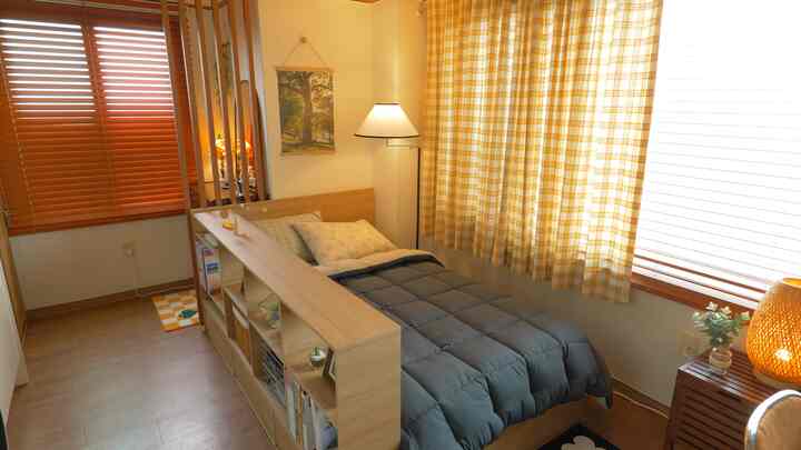 A cozy bedroom with warm wood tones and yellow check curtains, featuring a storage bed and bookshelf that define the unique layout