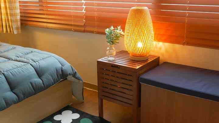 温かみのあるオレンジウッド調ブラインドと無垢材のサイドテーブル、ラタンランプが配された落ち着いた寝室空間