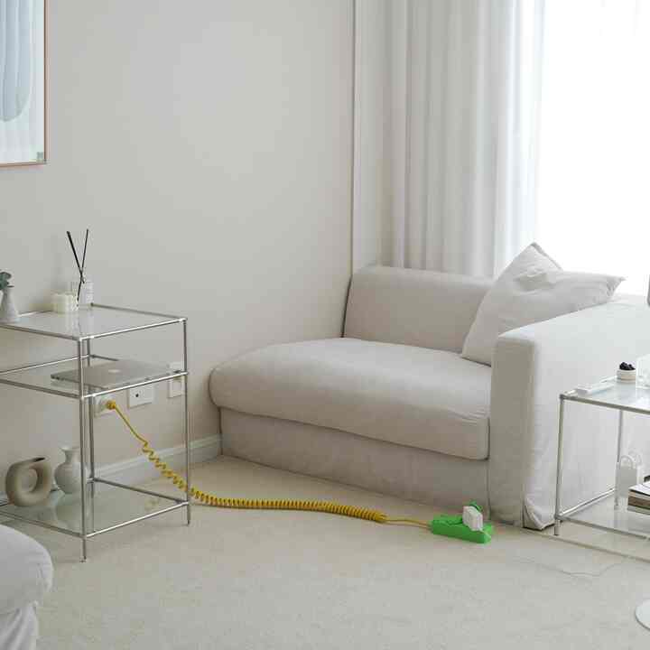 アイボリーとベージュのトーンのコンパクトなソファ空間、メタリックのサイドテーブルとシアーのシフォンカーテンが調和したシンプルなリビング