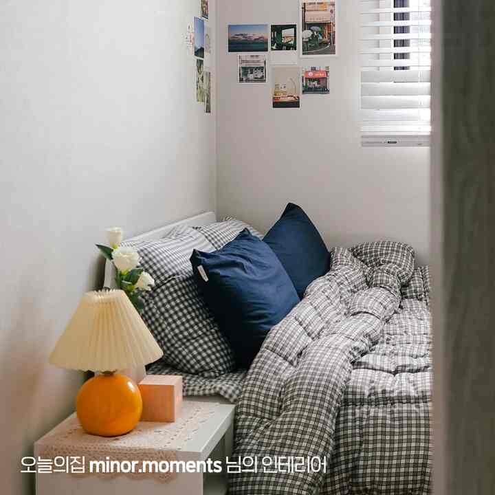 ホワイトの壁とネイビークッションが調和した6畳の寝室、シンプルなベッドとオレンジのテーブルランプが配置された落ち着いた印象的な空間