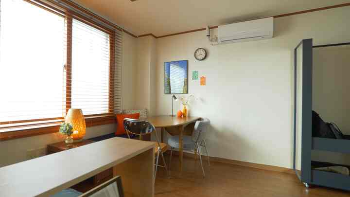 Bright white walls with wood tone floor and furniture define a single household workspace with mobile full-length mirror hanger and wood blinds by the window