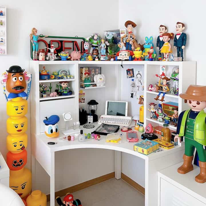 Bright, colorful home office with white corner desk featured centrally, adorned with numerous Toy Story character figurines on shelves and desk