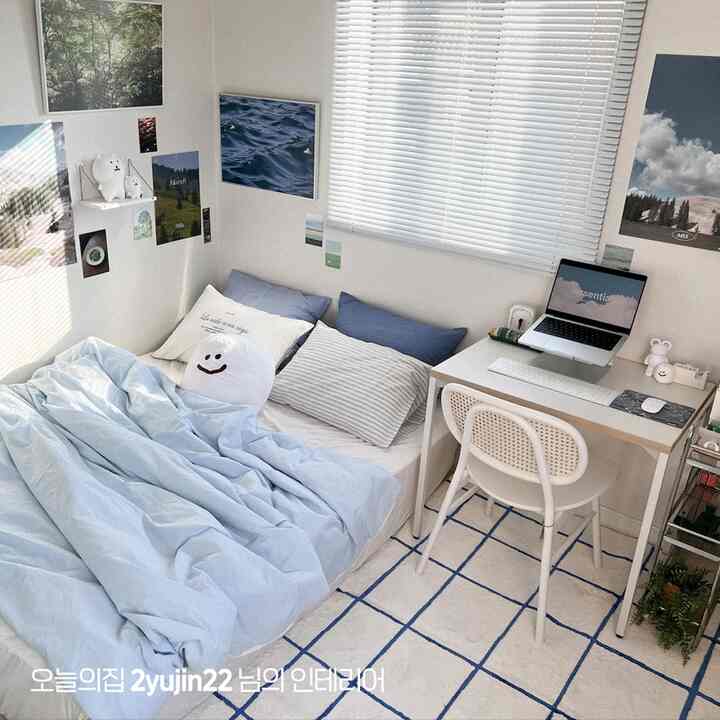 A small studio bedroom in white and blue tones featuring a simple natural home office with desk and bed