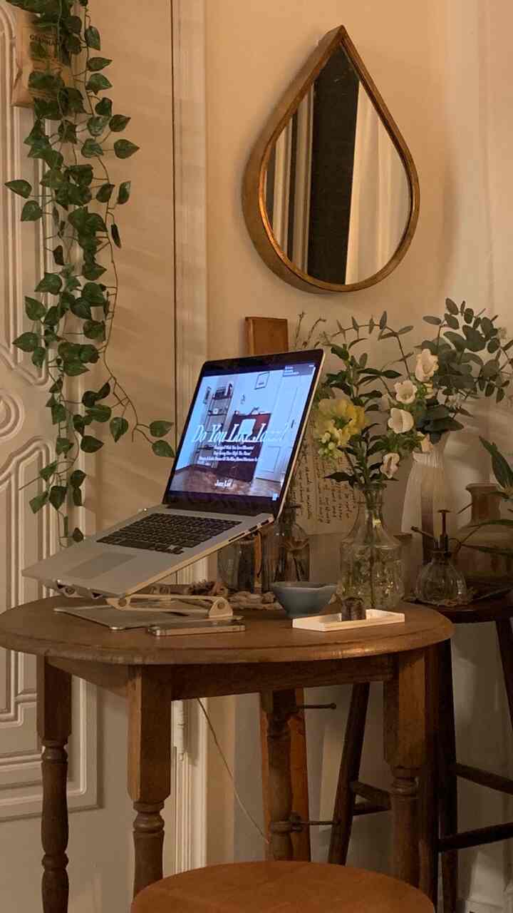 Natural home office space with warm beige walls and wooden table, featuring a laptop, vases, and a teardrop mirror creating a cozy atmosphere
