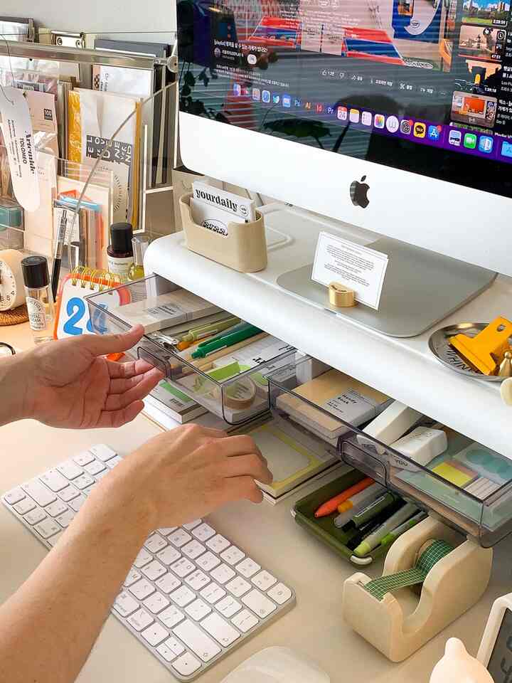 White-toned home office desk space featuring a monitor stand with clear drawers for organized storage