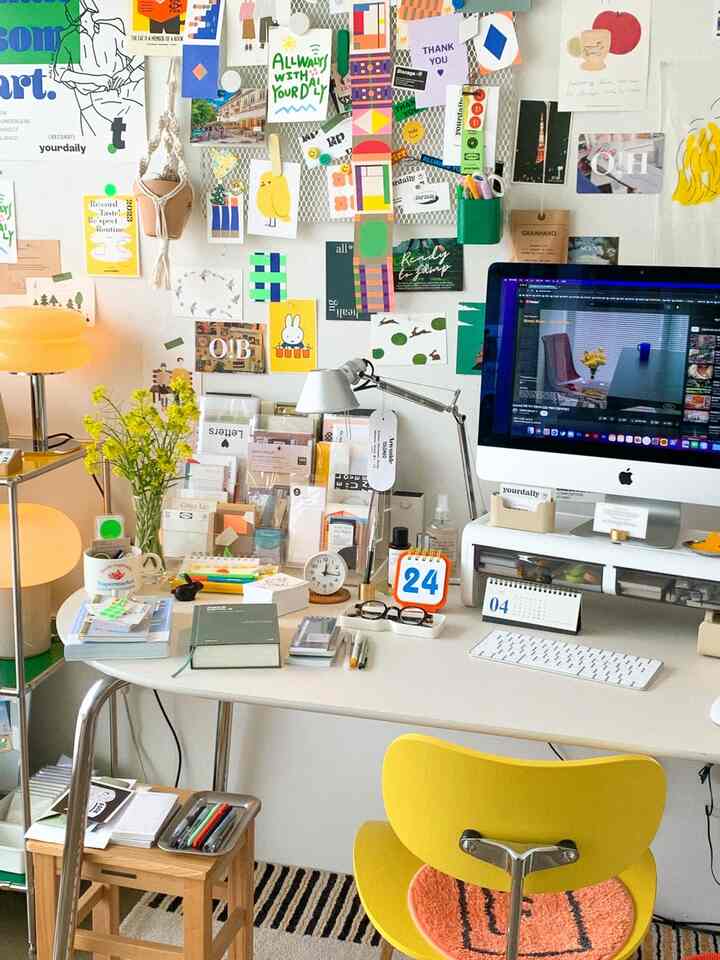 明るい黄色と白を基調としたワンルームのホームオフィス、デスクやパソコン、照明、多彩な壁の装飾が印象的なインテリア
