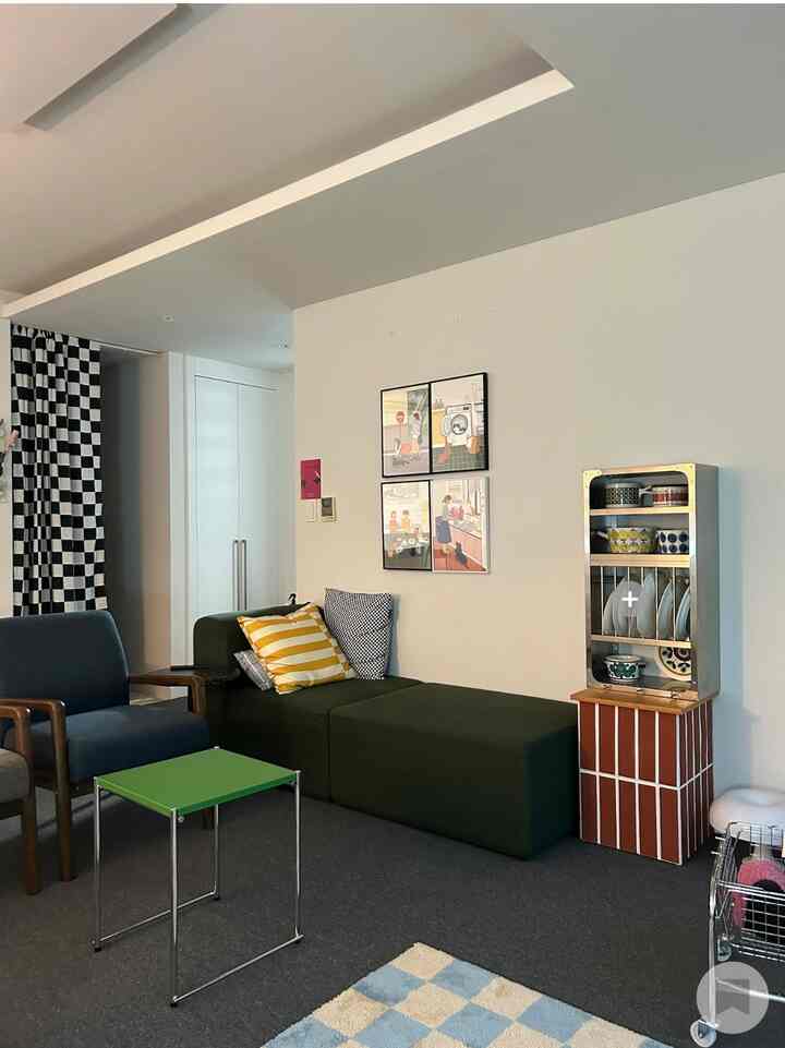 Simple living room with white walls and ceiling, featuring a green sofa and blue armchair, decorated with vintage dish objet