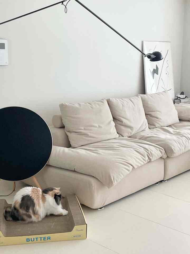 Beige and white toned living room featuring a large beige sofa and a cat scratching post on the floor, creating a cozy atmosphere
