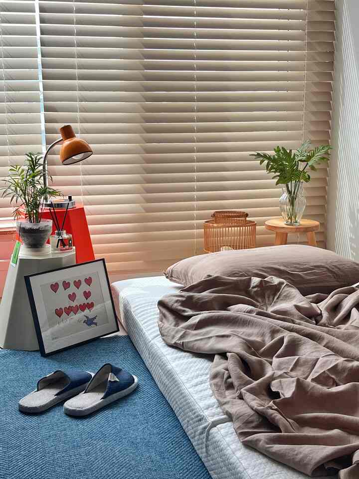 A natural-toned bedroom featuring beige wooden blinds, a neatly made mattress with brown bedding creating a cozy atmosphere