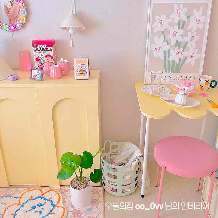 黄色とピンクのトーンの小さな部屋、黄色の収納キャビネットとテーブル、ピンクのスツール、モンステラの鉢が配置された印象的な空間