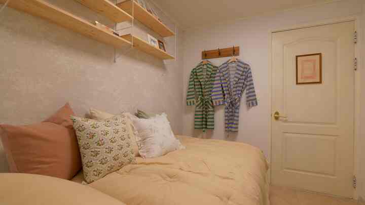 Beige-toned bedroom featuring a large sofa bed with multiple cushions and wooden wall hooks displaying couple robes, creating a warm and cozy atmosphere