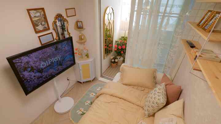 ホワイトとベージュの色調の寝室、可動式テレビ台とフロアランプ、白いレースカーテンと花瓶が配置された雰囲気のあるインテリア