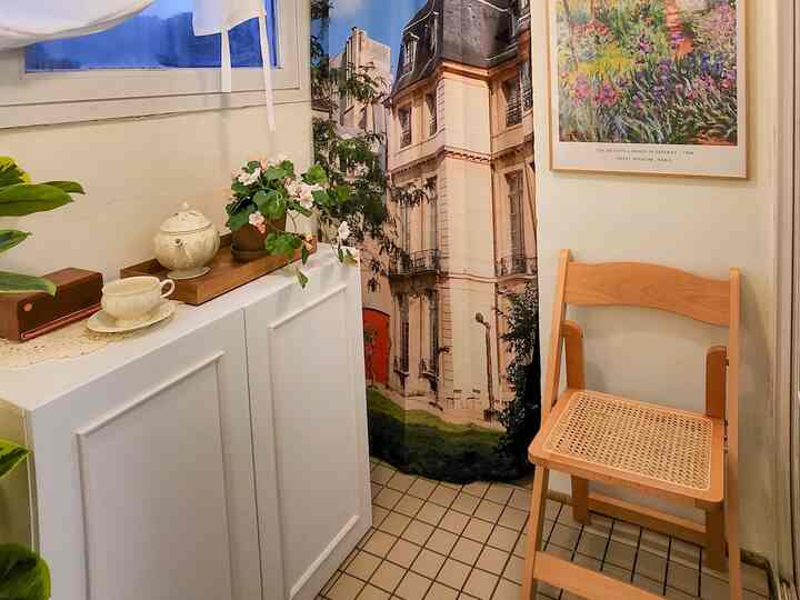 白とナチュラルカラーの小さなバルコニー、ラタンチェアとヨーロッパ風カーテンが配置された雰囲気のある空間