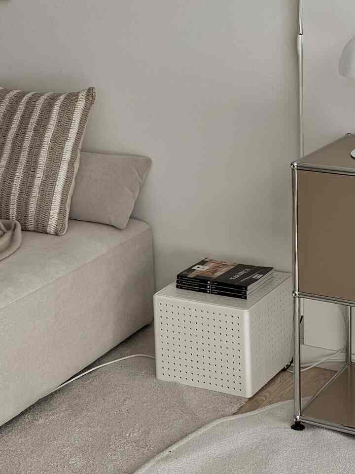 A beige and white toned living room featuring a white pegboard box nightstand next to a sofa and rug, presenting a natural and modern space