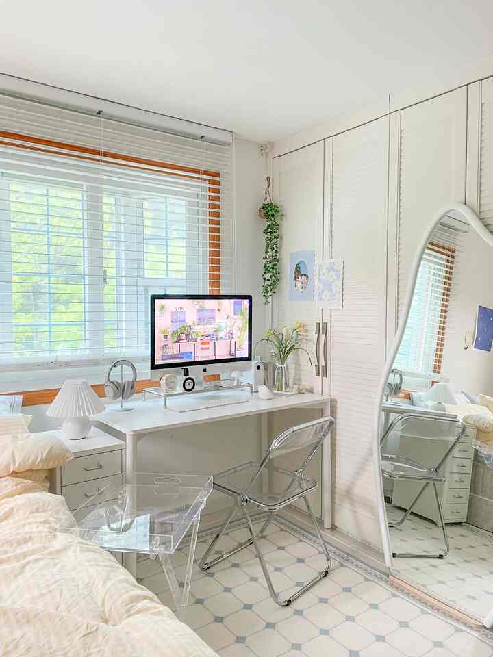 A clean, modern bedroom and home office with white and beige tones featuring transparent furniture