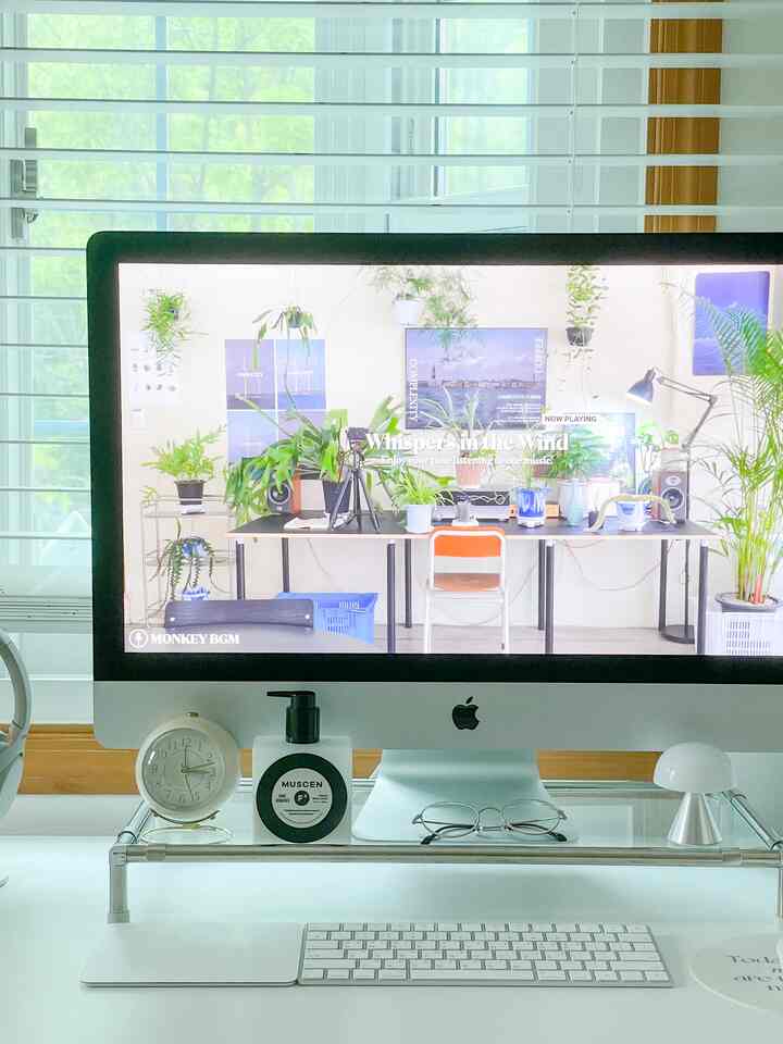 White and silver toned home office featuring a transparent monitor stand holding an iMac in a clean workspace