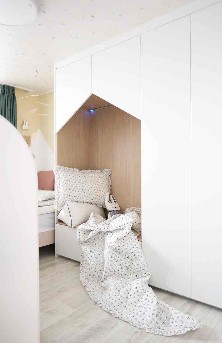 白と木目調が調和した子供部屋、壁面収納内に夏用寝具やクッション、モビールが配置された雰囲気のある空間