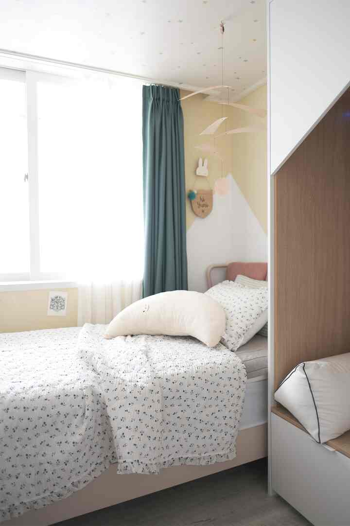 Bright bedroom with white walls and mint curtains, featuring a child's bed and decorative mobile creating a cozy atmosphere