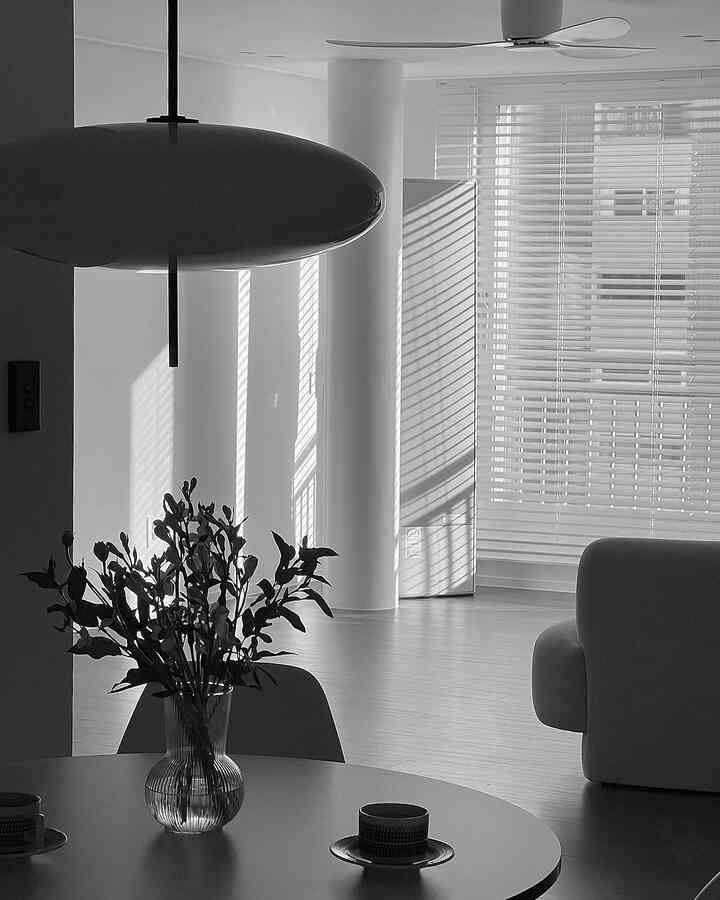 白と黒のモノトーンリビング、大きなペンダントライトと木製ブラインド、丸いテーブルに花瓶が置かれたシンプルなインテリア