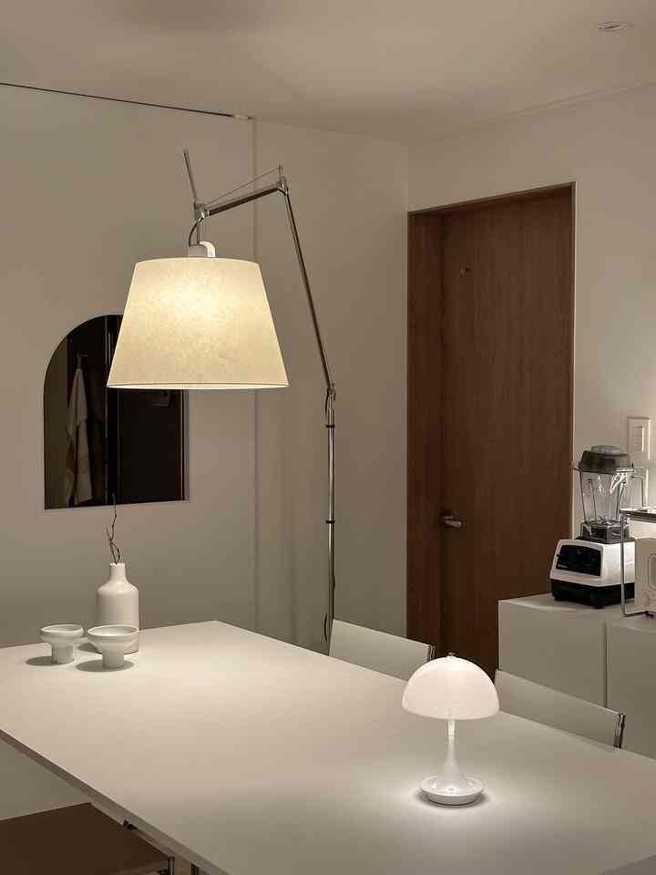 White and natural toned dining room featuring an Artemide floor lamp and Louis Poulsen table lamp in a modern setting