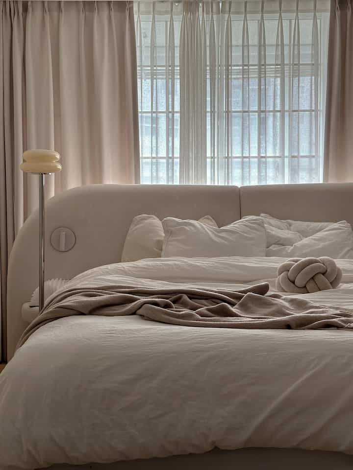 柔らかいベージュ色調の寝室、中央にふかふかのベッドとスタンドランプが配置された居心地の良い空間