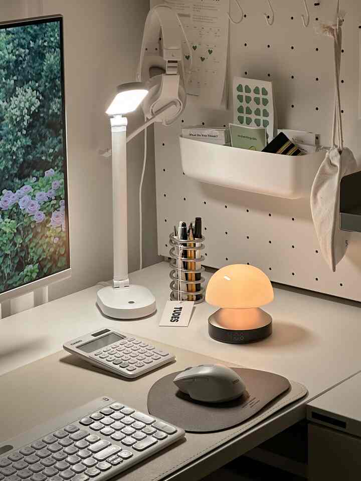 ホワイトトーンのコンパクトなホームオフィス、照明と目覚まし時計が置かれた整然としたデスク