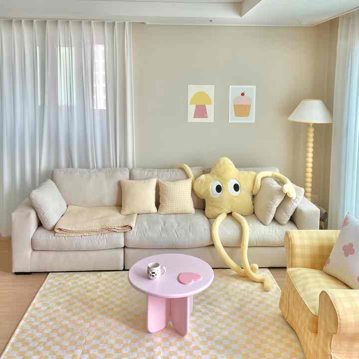 Living room in soft beige and yellow tones featuring a beige sofa, bright yellow plush toy, and a checkered rug creating a cozy atmosphere